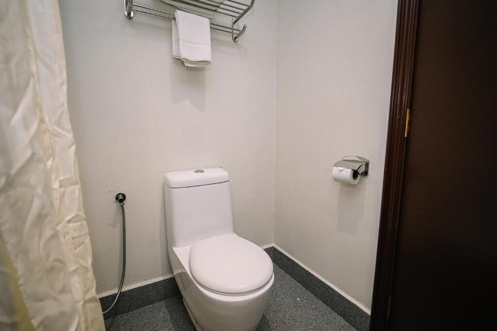 A small, clean bathroom with a toilet, a shower hose, and a toilet paper holder.