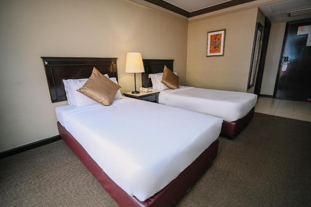 Una habitación de hotel con dos camas, una mesita de noche con lámpara y un cuadro enmarcado en la pared.