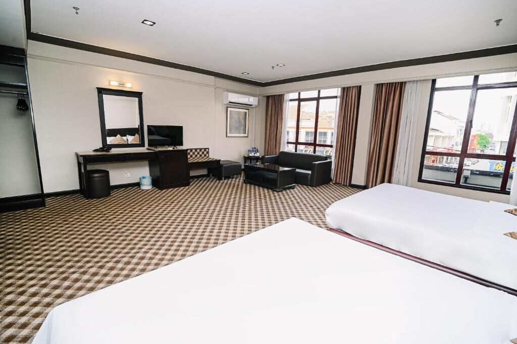 Una habitación de hotel con piso a cuadros, una cama, un escritorio con computadora, una silla, un televisor y un amplio ventanal con cortinas.