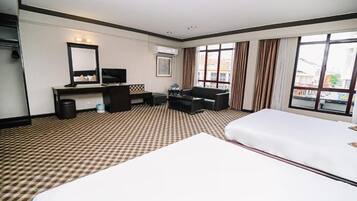 Una habitación de hotel con piso a cuadros, una cama, un escritorio con computadora, una silla, un televisor y un amplio ventanal con cortinas.