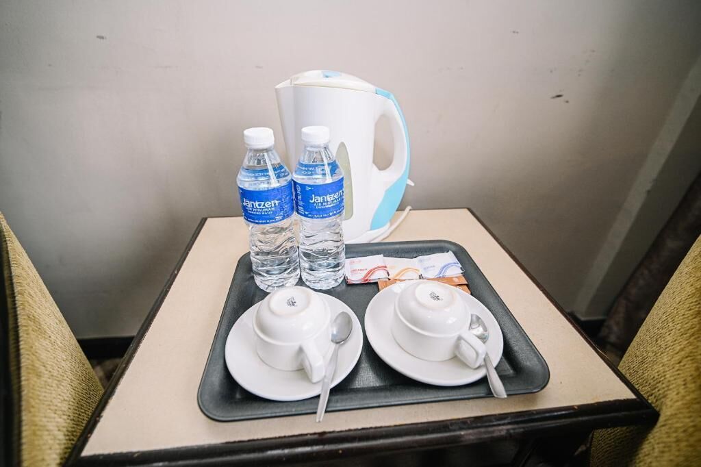 Un plateau avec deux bouteilles d’eau, une théière blanche, deux tasses blanches et une cuillère, posés sur une petite table.