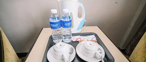Un plateau avec deux bouteilles d’eau, une théière blanche, deux tasses blanches et une cuillère, posés sur une petite table.
