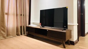 Un televisor de pantalla plana sobre un soporte de madera en una habitación con cortinas color beige y suelo de madera.