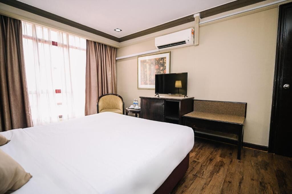 A hotel room with a large bed, a desk with a chair, a television, and an air conditioning unit.