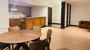 Una sala de estar moderna con una mesa de comedor redonda de madera y sillas, una cocina con armarios de madera, y un ventanal grande.