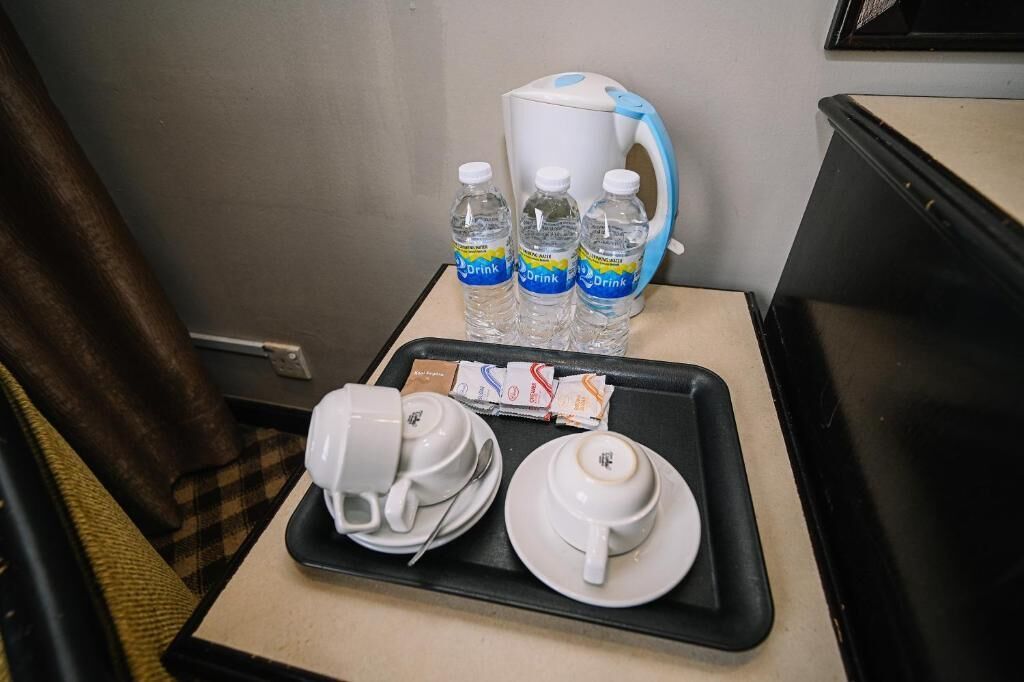 A hotel room with a small table featuring a kettle, three water bottles, a tray with two cups and a saucer, and some packets.