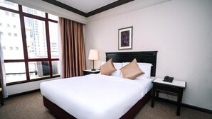 Habitación de hotel con una cama grande, una mesita de noche con lámpara, tel éfono y ventana con cortinas.