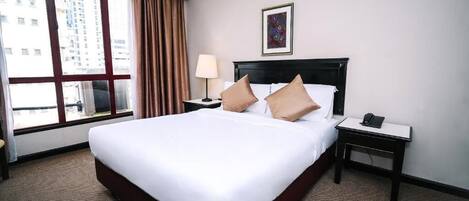 A hotel room with a large bed, a nightstand with a lamp, a phone, and a window with curtains.