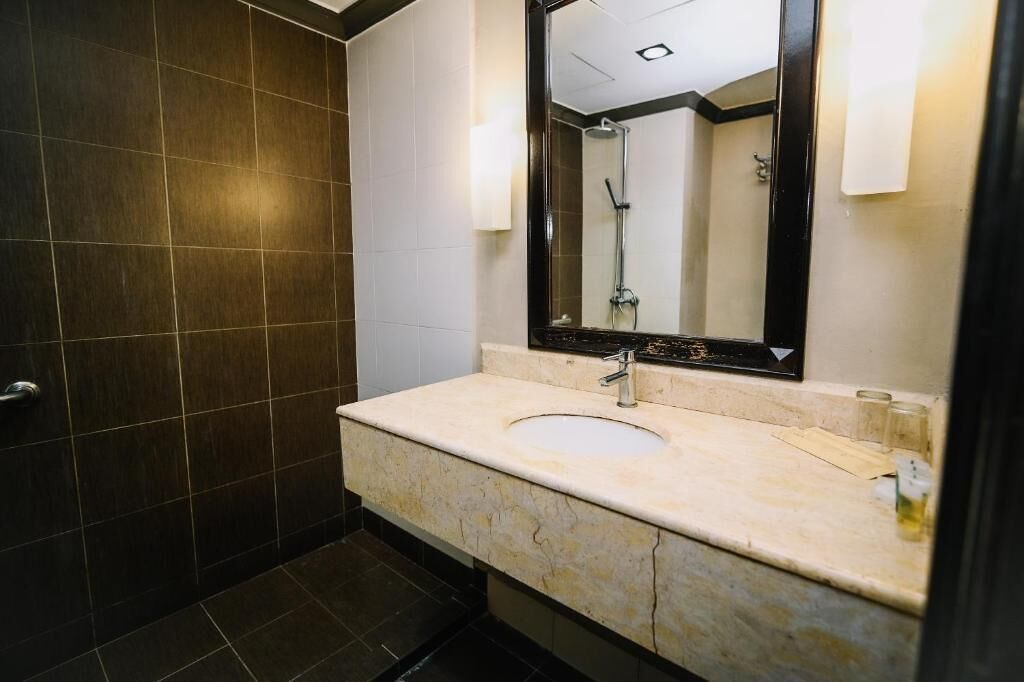 Une salle de bain moderne avec un mur recouvert de carreaux foncés, un lavabo en marbre beige et un grand miroir.