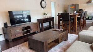 A living room with a TV, wooden furniture, a dining area with chairs, and a kitchen in the background. - Hahndorf Retreat Cottage (Hahndorf)