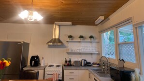 A kitchen with wooden ceiling, stainless steel range hood, white cabinets, and a window with a view of greenery. - Hahndorf Retreat Cottage (Hahndorf)