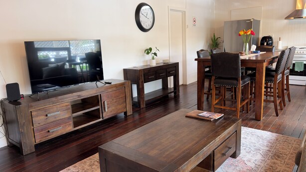 A living room with a TV, wooden furniture, a dining area, and a kitchen. - Hahndorf Retreat Cottage (Hahndorf)