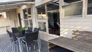 An outdoor deck with a table and chairs, a wicker sofa, and a potted plant. - Hahndorf Retreat Cottage (Hahndorf)