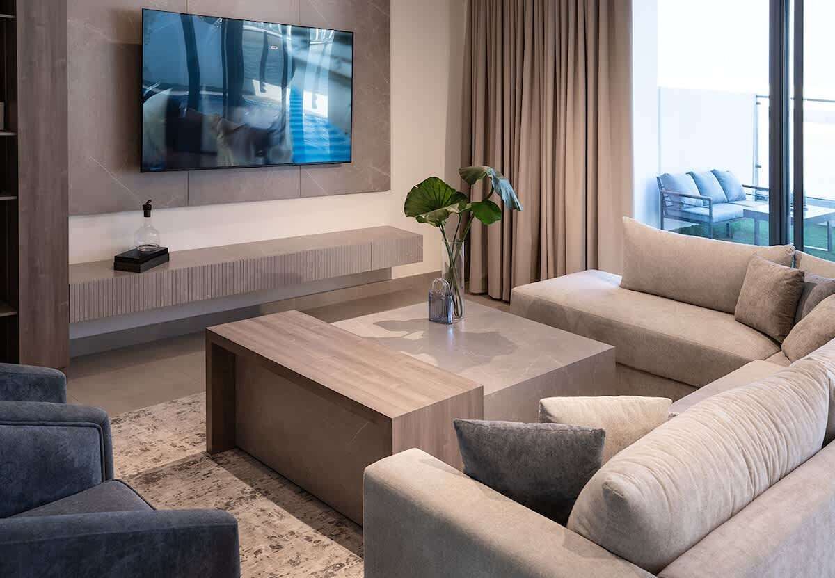 A modern living room with a flat-screen TV mounted on the wall, a coffee table, sofas, and a plant.