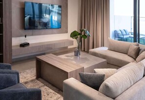 Ein modernes Wohnzimmer mit einem wandmontierten Flachbildfernseher, einem Couchtisch, Sofas und einer Pflanze.