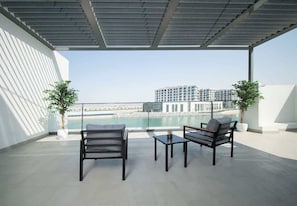 Ein Balkon mit zwei Stühlen und einem Tisch, mit Blick auf ein Gewässer und Gebäude.