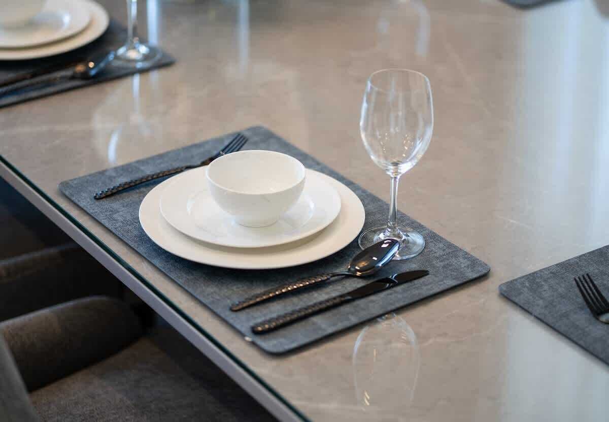 A table set with a white bowl, plate, wine glass, and cutlery on a grey placemat.