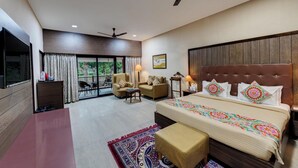 A spacious bedroom with a large bed, a ceiling fan, a TV, and a balcony with a view of greenery. - Royal Safari Lakeside Resort- Little Rann of Kutch (Dasada)