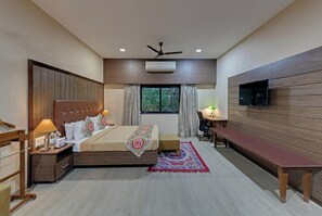 A modern hotel room with a bed, bedside table, desk, chair, and a TV mounted on the wall. - Royal Safari Lakeside Resort- Little Rann of Kutch (Dasada)