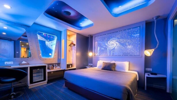 Une chambre d’hôtel moderne dotée d’un grand lit, d’un bureau, d’une chaise et d’un plafond agrémenté d’un éclairage original.