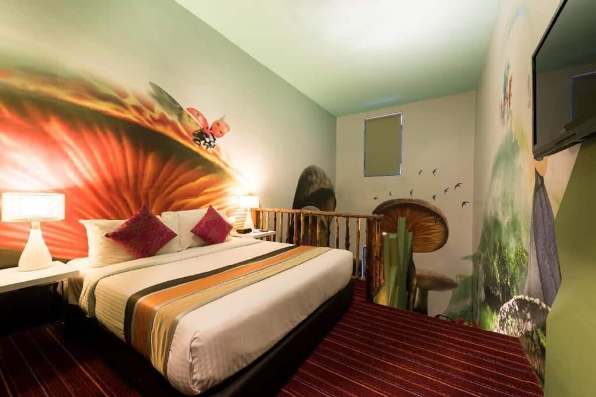 Habitación de hotel con una cama, una mesita de noche, una lámpara, una barandilla de madera y un mural en la pared.