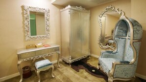 Une pièce comprenant une coiffeuse, un grand miroir, une armoire et un fauteuil bleu recouvert de tissu.