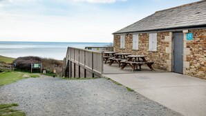 Un bâtiment en pierre doté d  ’une terrasse en bois et de tables de pique-nique, le tout offrant une vue sur la mer.