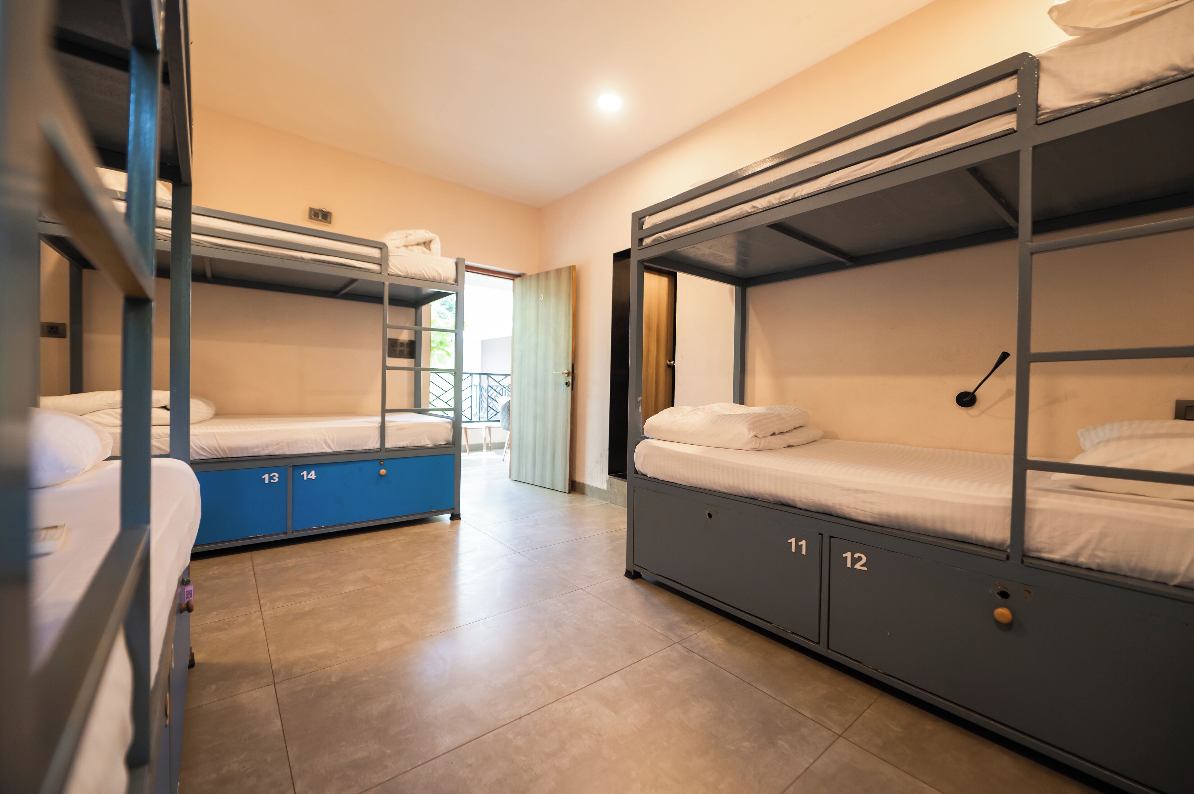 A dormitory room with bunk beds, numbered storage compartments, and a view through an open door.