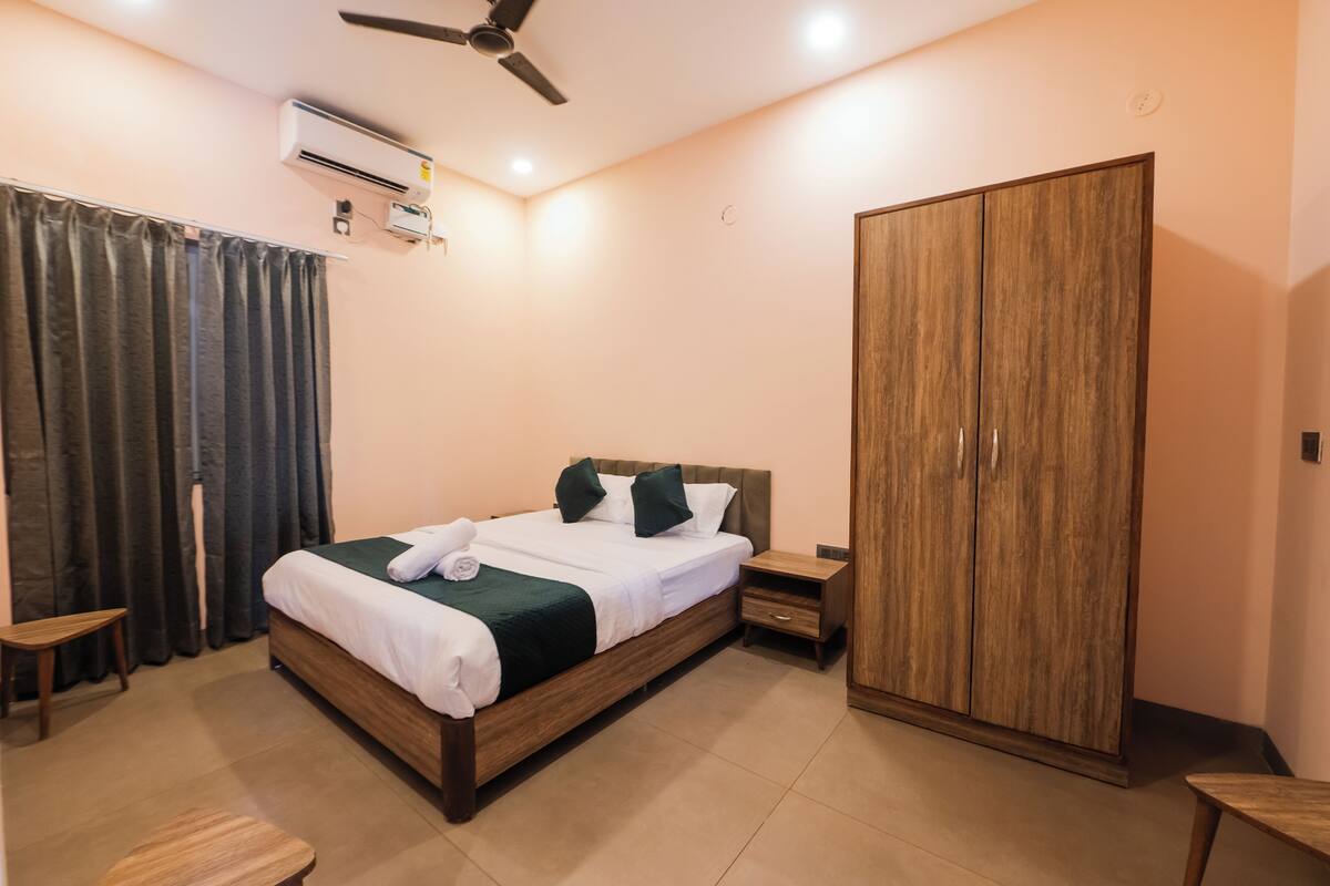 A bedroom with a bed, a wardrobe, a nightstand, a small table, and an air conditioning unit.