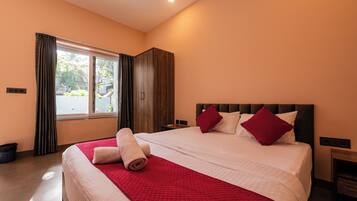 Una habitación de hotel con una cama grande, un armario, una ventana con cortinas y una mesita de noche.