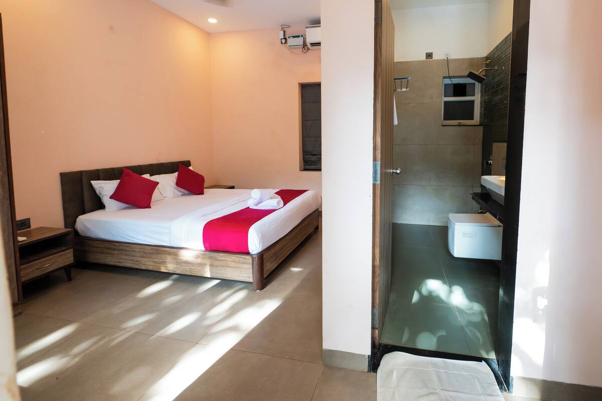 A modern hotel room with a large bed, a bedside table, a ceiling fan, and a view into the bathroom.