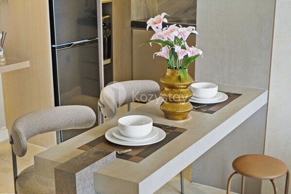 Un comedor moderno con una mesa larga, dos sillas, un florero con flores y un tazón.