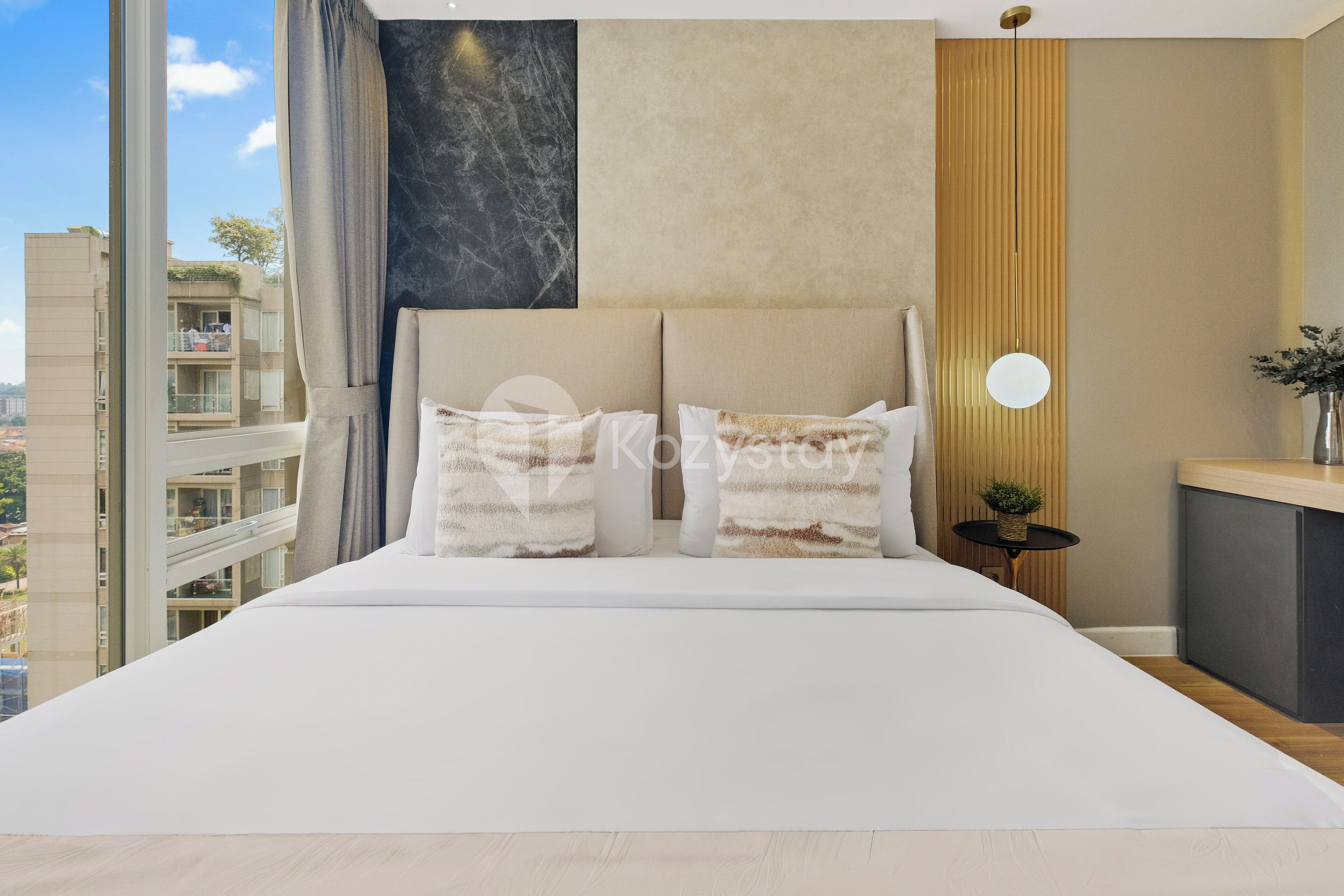Een moderne slaapkamer met een groot bed, uitzicht op de stad en een klein tafeltje met een plant.