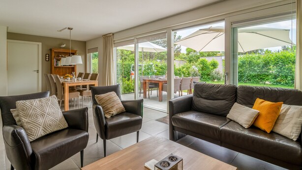 A modern living room with leather sofas, a wooden coffee table, and a dining area with a table and chairs. Large windows provide a view of the garden. - Tastefully Furnished Country House for 6 People (Den Burg)