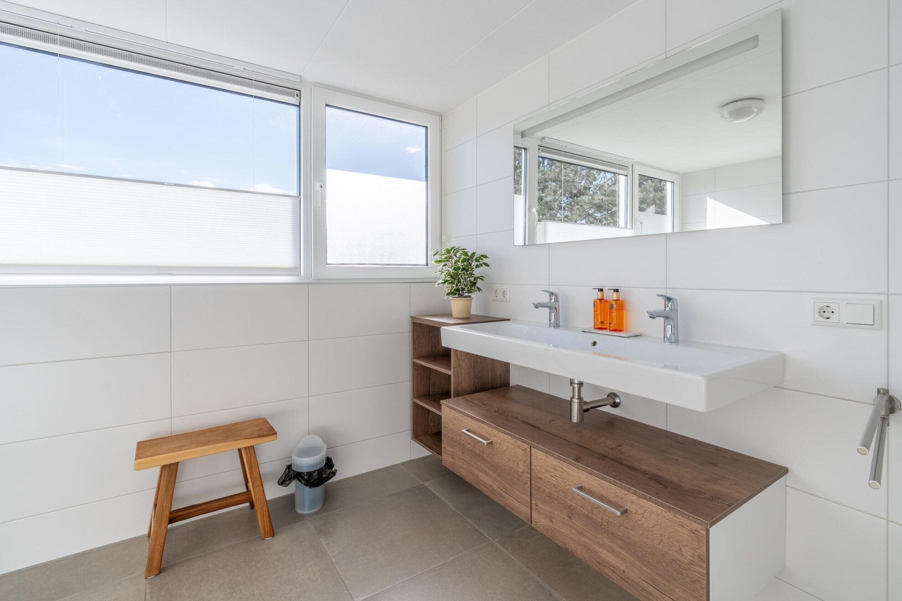 A modern bathroom with a wooden vanity, white sink, and a large mirror.