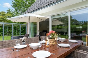 An outdoor dining area with a wooden table set for four, surrounded by wicker furniture and large umbrellas. - Tastefully Furnished Country House for 6 People (Den Burg)