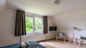A bedroom with a bed, a window with curtains, a chair, a table, and a television. - Tastefully Furnished Country House for 6 People (Den Burg)
