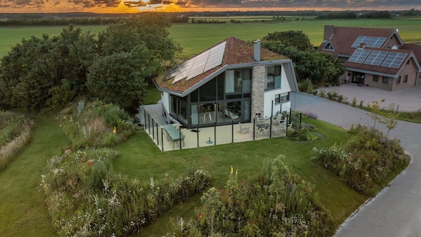 A modern house with a large glass facade, a spacious patio, and solar panels on the roof. - Modern, Luxurious, Sustainable Nature Villa With hot tub and Texel View (De Waal)