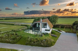 Uma casa moderna com fachada envidraçada ampla, cercada por um jardim bem cuidado e vista para o campo.