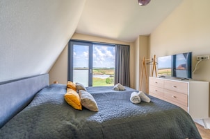 Quarto com cama grande, televisão, penteadeira e vista para uma paisagem pela janela.