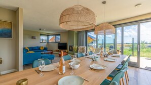 A dining area with a long wooden table set for six, surrounded by green chairs. There are two large woven pendant lights above the table. - Modern, Luxurious, Sustainable Nature Villa With hot tub and Texel View (De Waal)