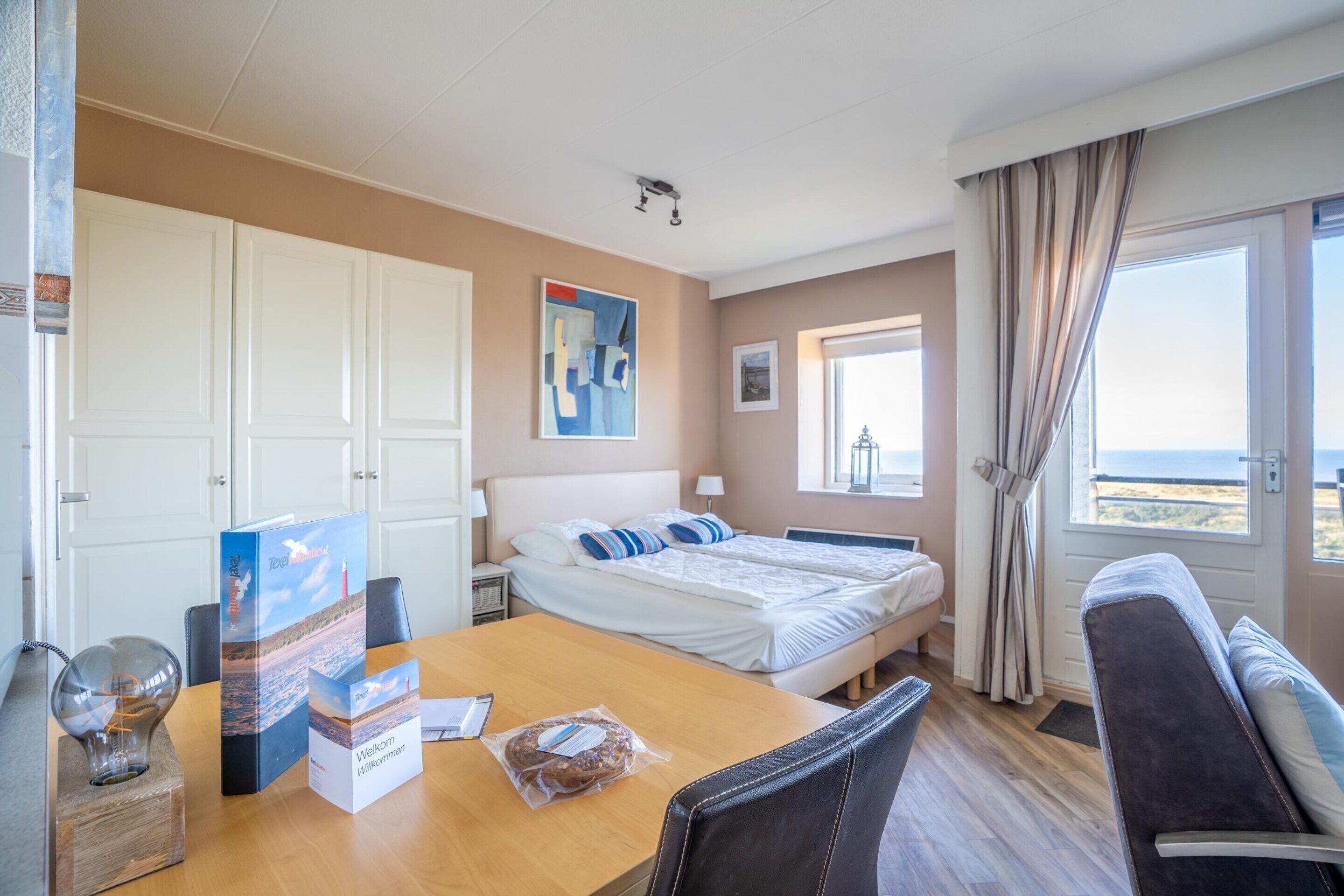 Ein Hotelzimmer mit Bett, Schreibtisch mit Laptop, Stuhl, Sofa und Blick aufs Meer.