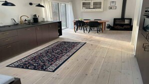 Moderni keittiö, jossa on tummat kaapit, ruokailutila puupöydällä ja -tuoleilla, suuri matto ja puukamiina.