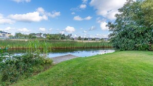 Een gazon met een vijver, omgeven door groen en huizen op de achtergrond.
