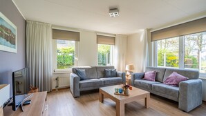 Een moderne woonkamer met twee grijze banken, een houten salontafel en een televisie op een houten dressoir.
