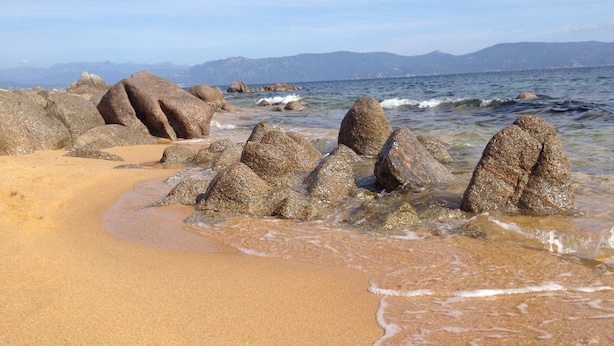 Ein Strand mit großen Felsen im Wasser und einem sandigen Ufer.