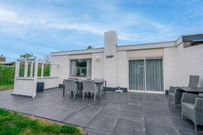 Une maison moderne dotée d’un patio comprenant une table et des chaises, une façade en briques blanches et une porte-fenêtre coulissante.