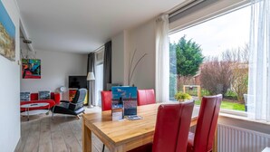 A dining area with a wooden table and red chairs, a red sofa, and a view of greenery outside. - Cozy and Comfortable 4-person Bungalow (De Koog)