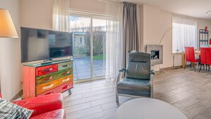 A living room with a TV, a fireplace, a red sofa, and a dining area with red chairs. - Cozy and Comfortable 4-person Bungalow (De Koog)