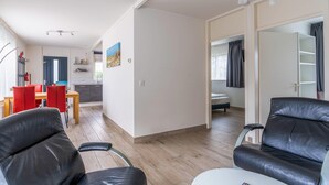 A modern living room with leather chairs, a dining area with red chairs, and a kitchen in the background. - Cozy and Comfortable 4-person Bungalow (De Koog)
